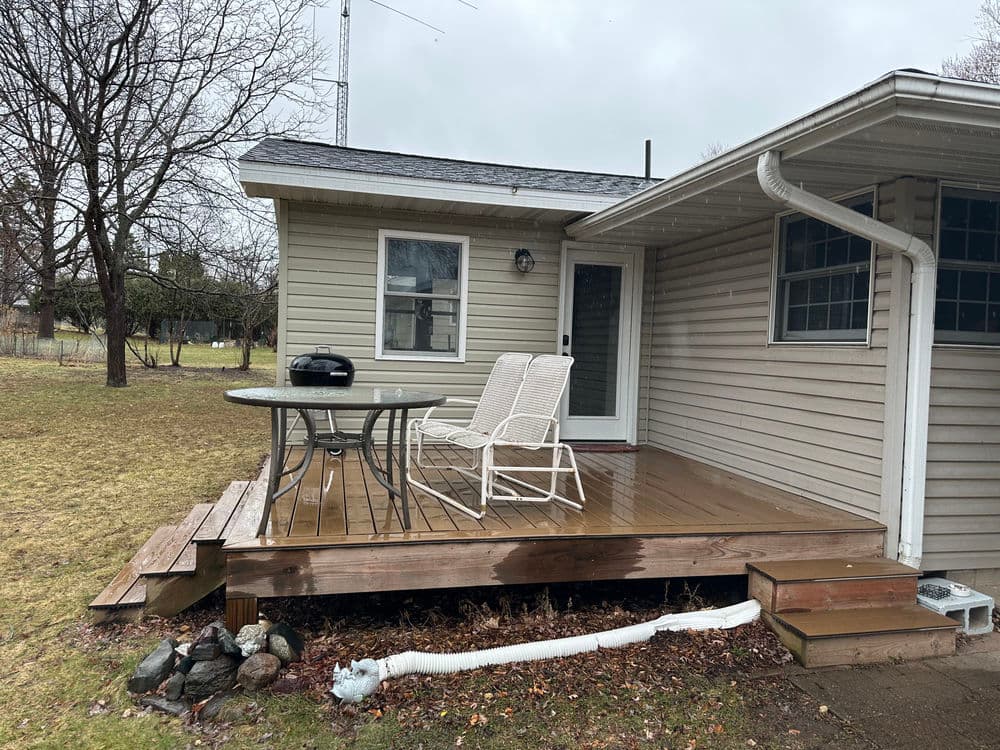 Wooden deck with chairs and table beside a house on a cloudy day.