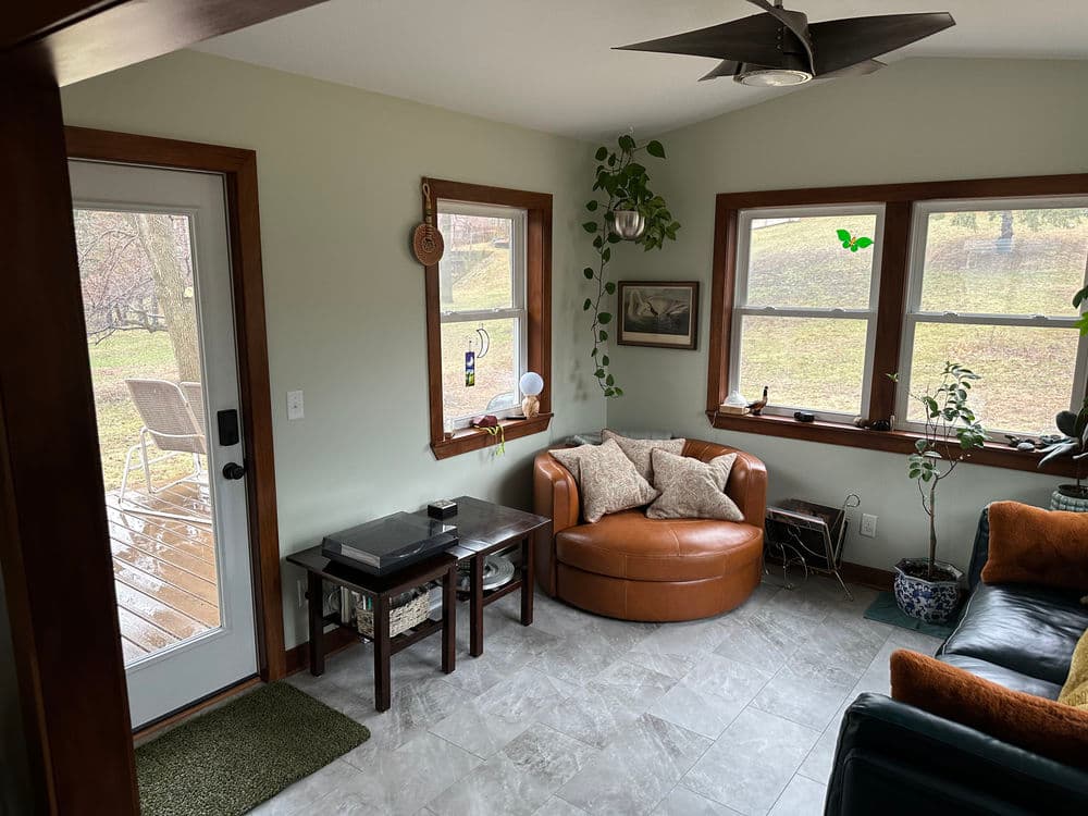Cozy living room with a brown chair, potted plants, and natural light from windows.