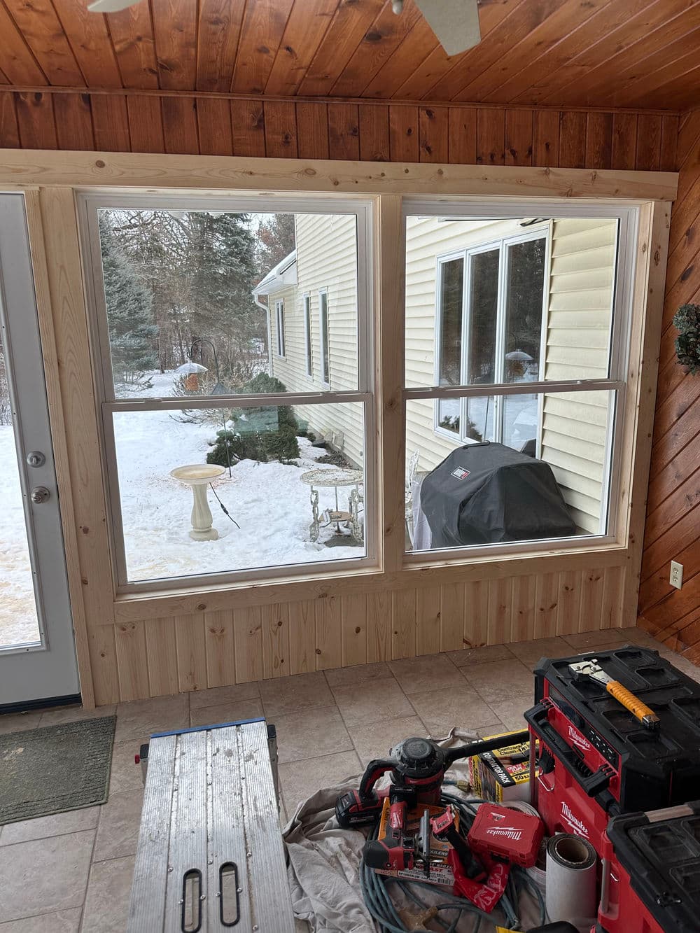 Newly installed window in a cozy sunroom overlooking a snowy outdoor scene. Construction tools visible.