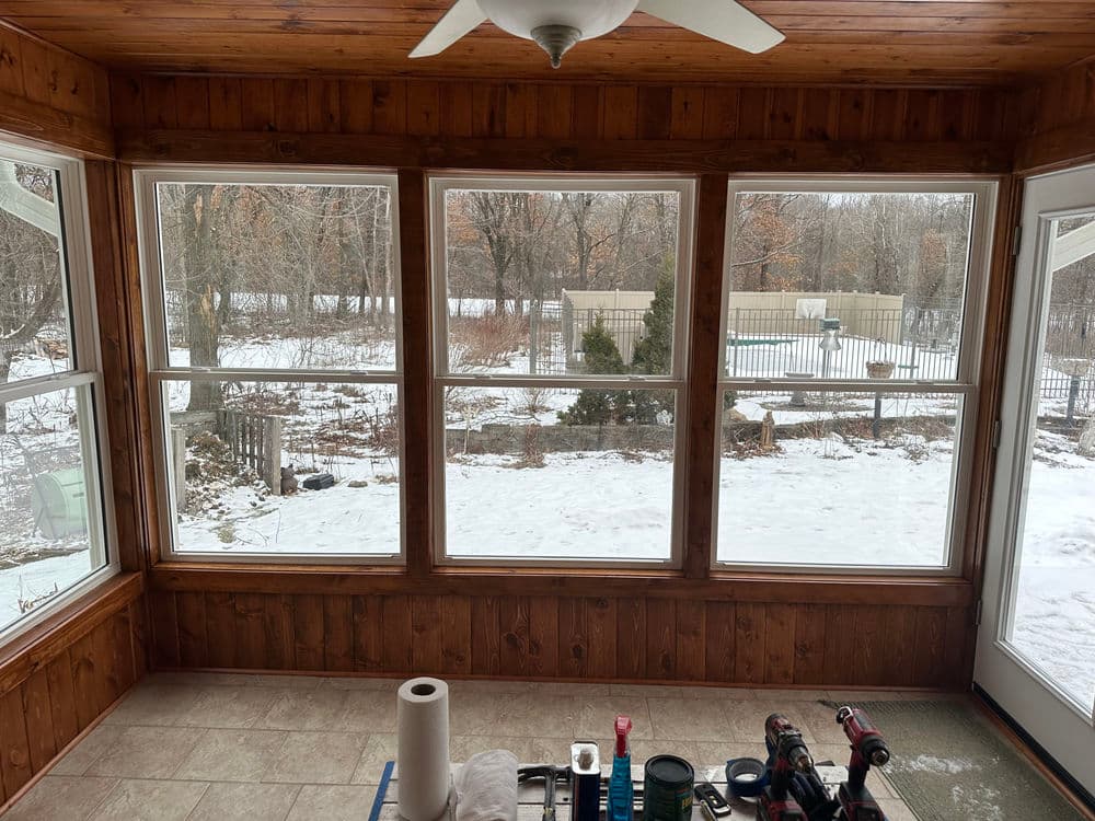 Sunroom with large windows overlooking a snowy landscape and wooden paneling.