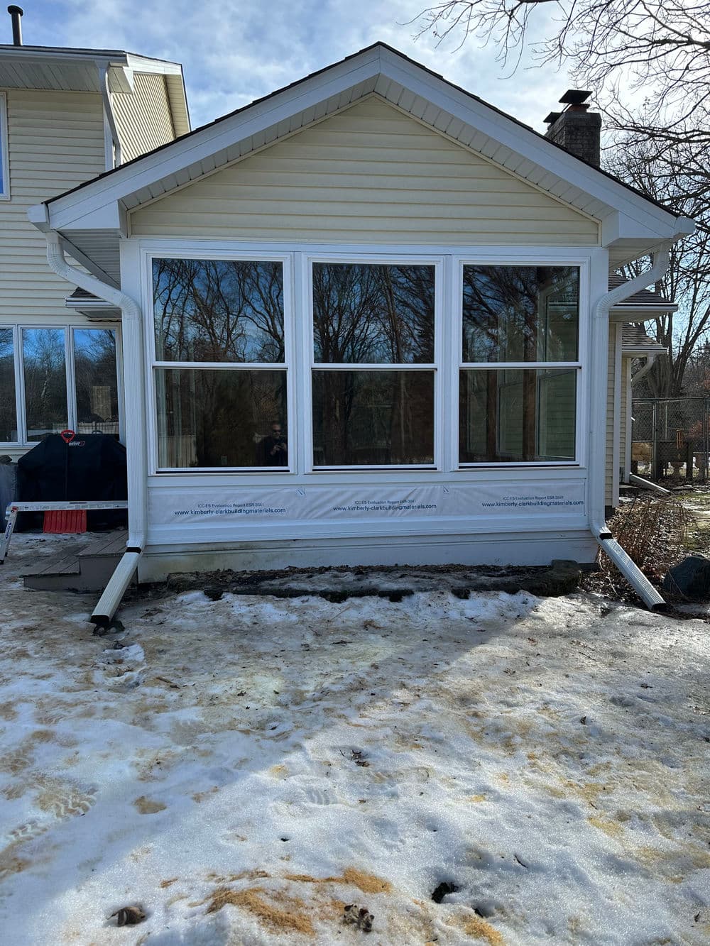 Front view of a house with large windows, snow on the ground, and construction materials visible.