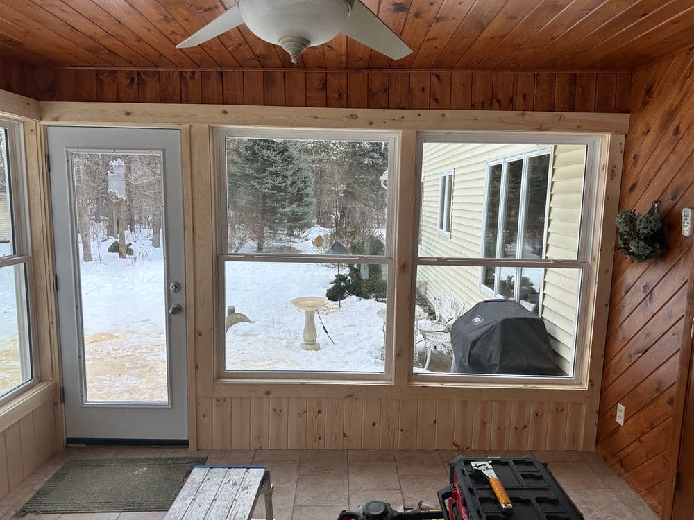 Cozy sunroom with large windows overlooking snowy landscape and outdoor grill.
