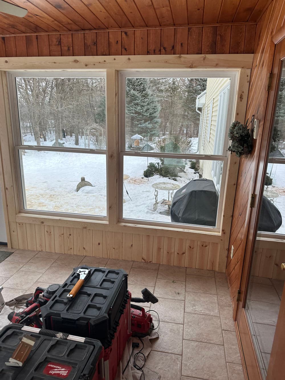 View of a sunroom with snow outside, tools on the floor, and a barbecue grill visible.