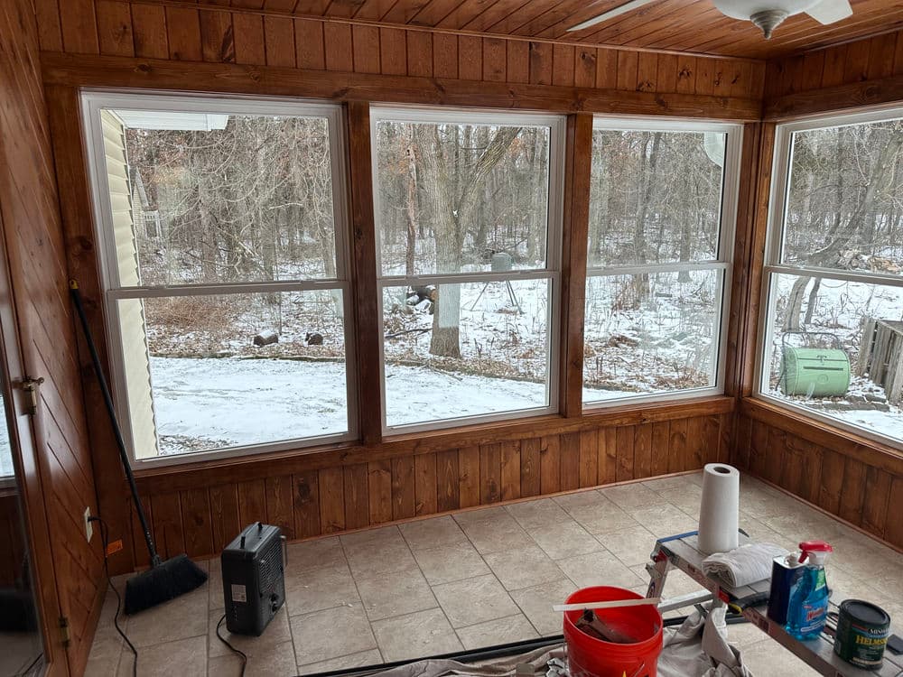 Sunroom with wooden walls and tiled floor, featuring snow-covered trees outside.
