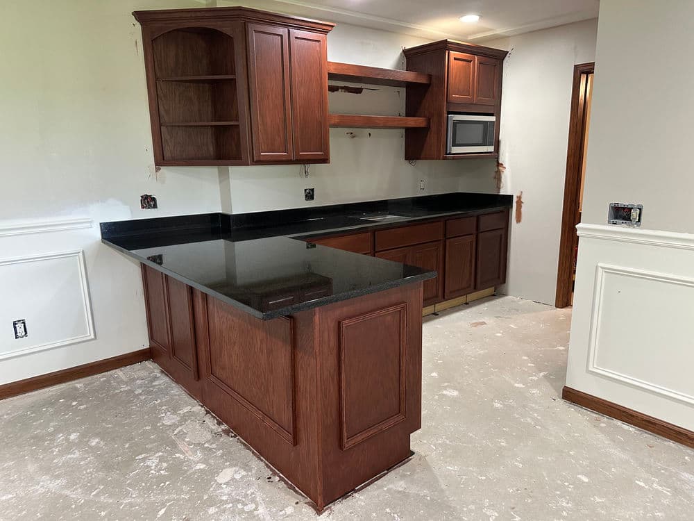 Modern kitchen with dark wood cabinets, black countertops, and microwave in a renovation setting.