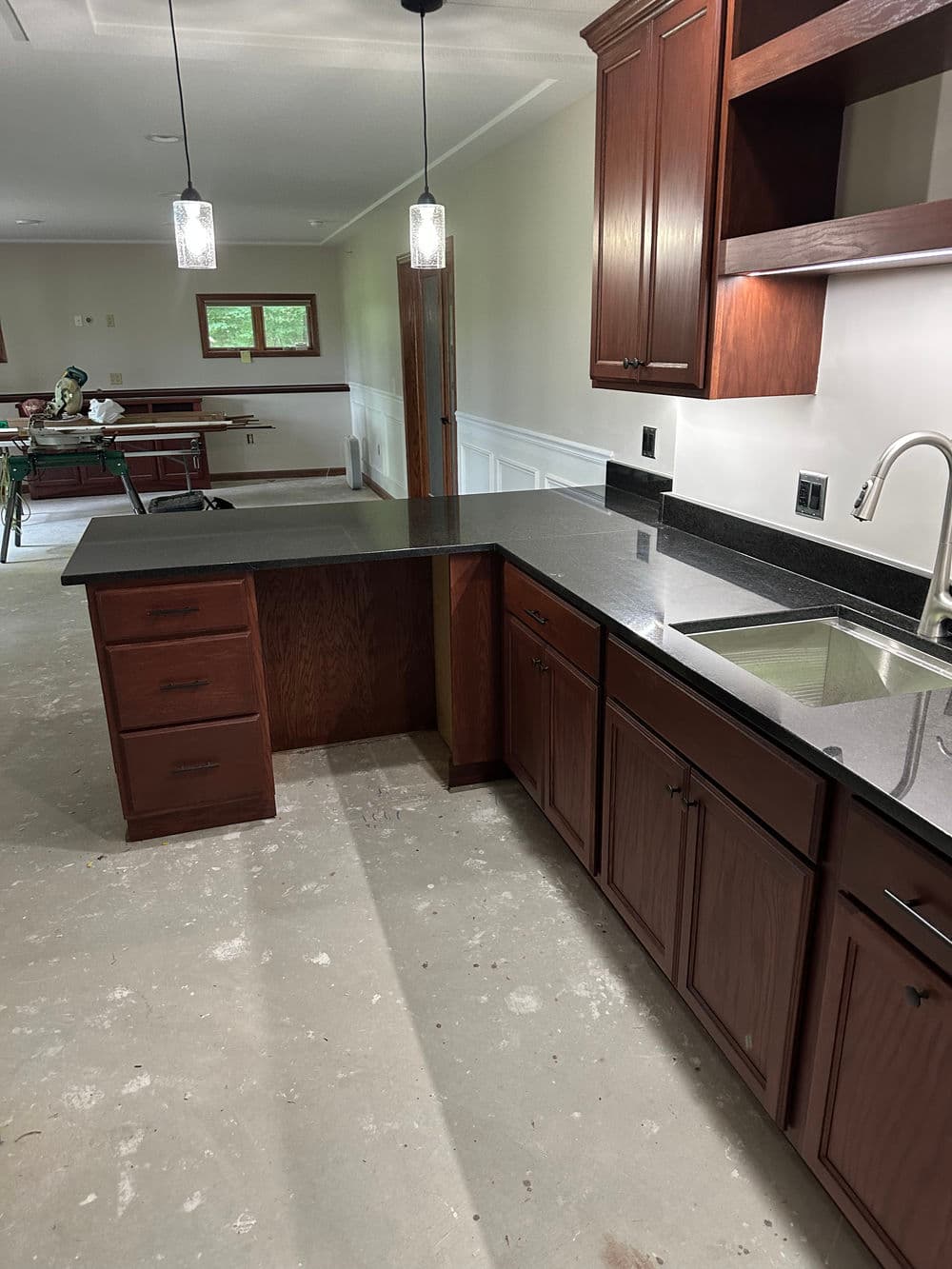 Modern kitchen with dark wood cabinets and sleek countertop, under pendant lighting.