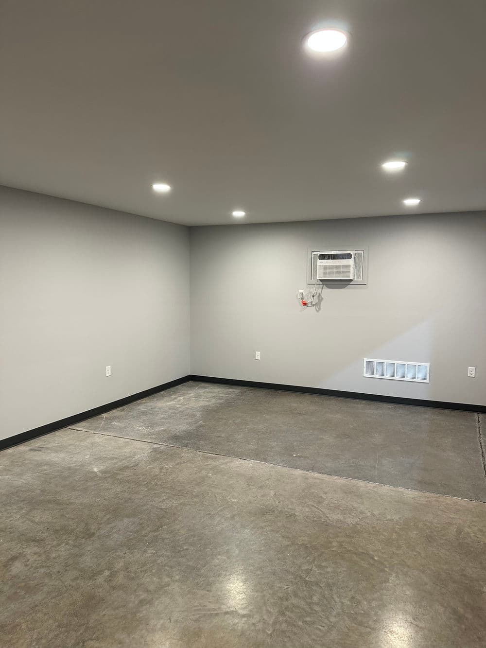 Empty modern garage space with gray walls, polished concrete floor, and air conditioning unit.
