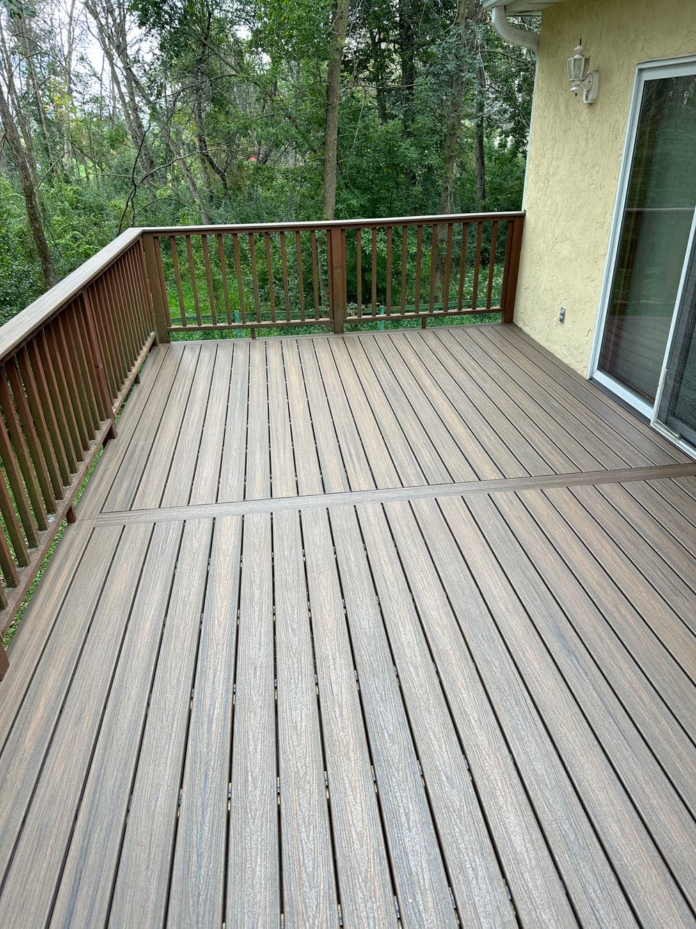 Newly installed wooden deck with railings overlooking a lush green wooded area.