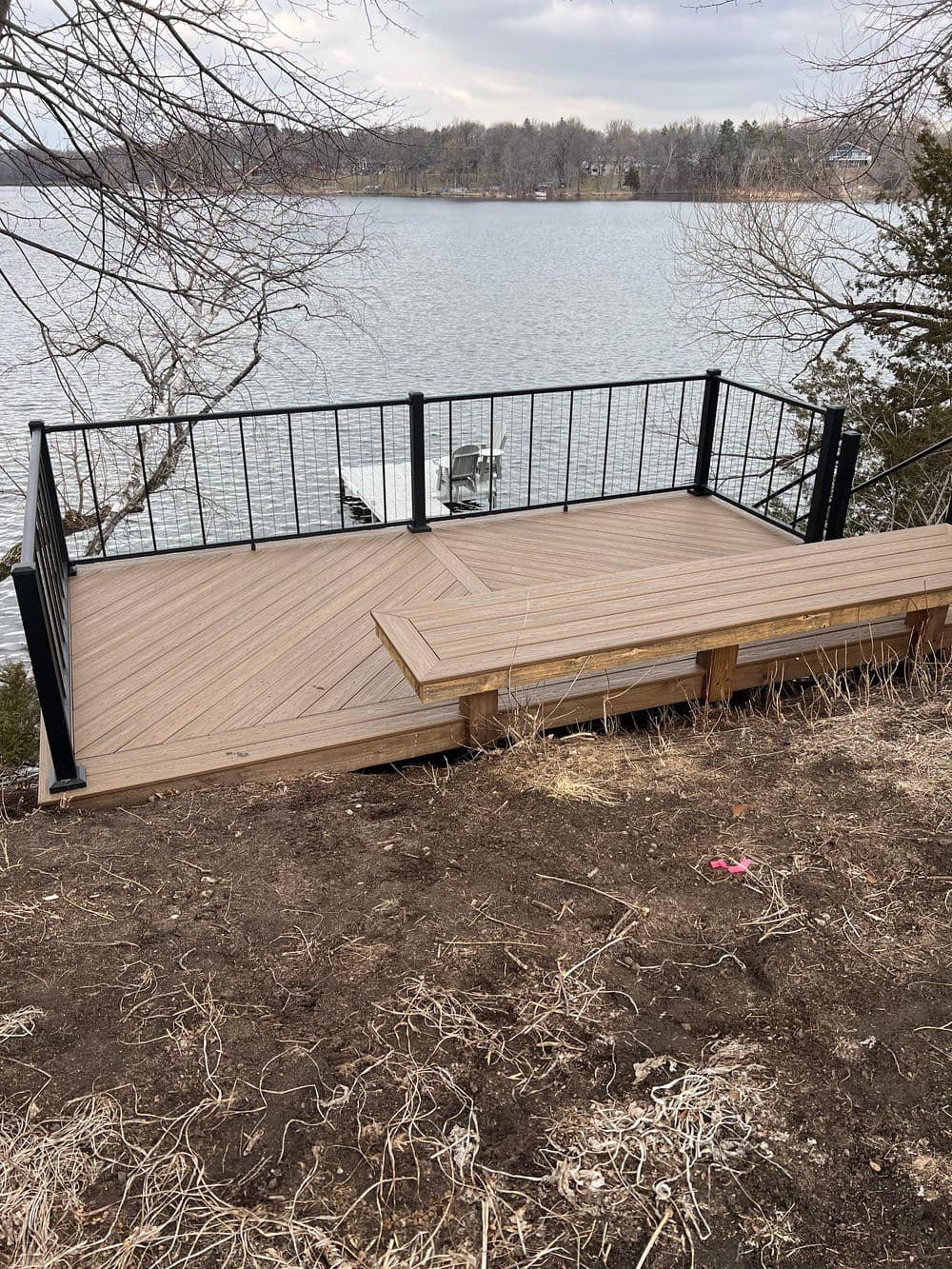 Wooden deck overlooking a serene lake with black railings and natural landscaping.
