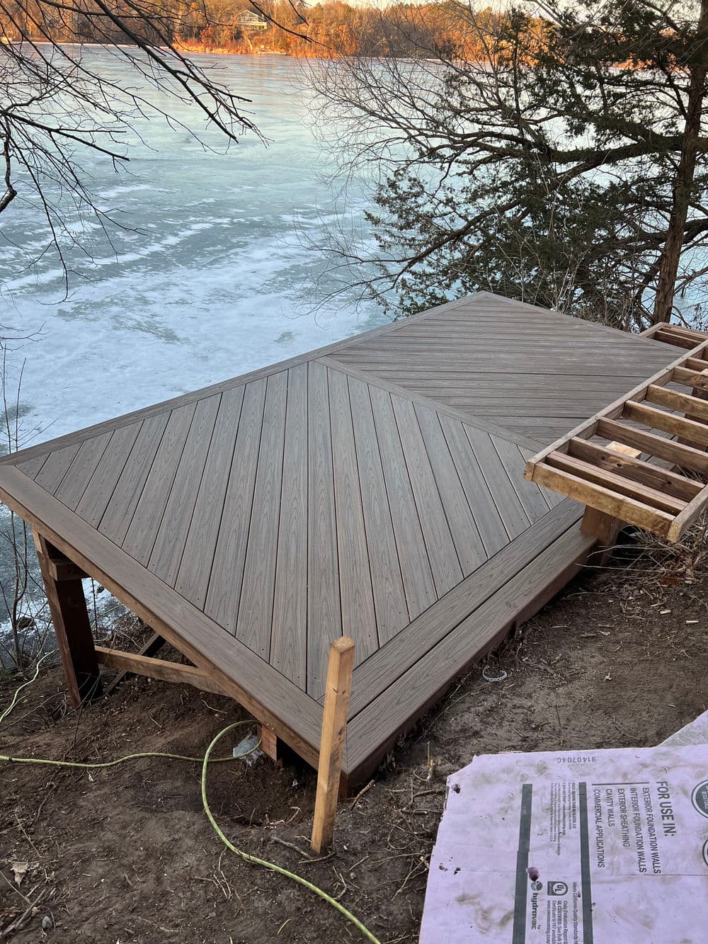 Newly constructed wooden deck by frozen lake, showcasing unique diagonal plank pattern.