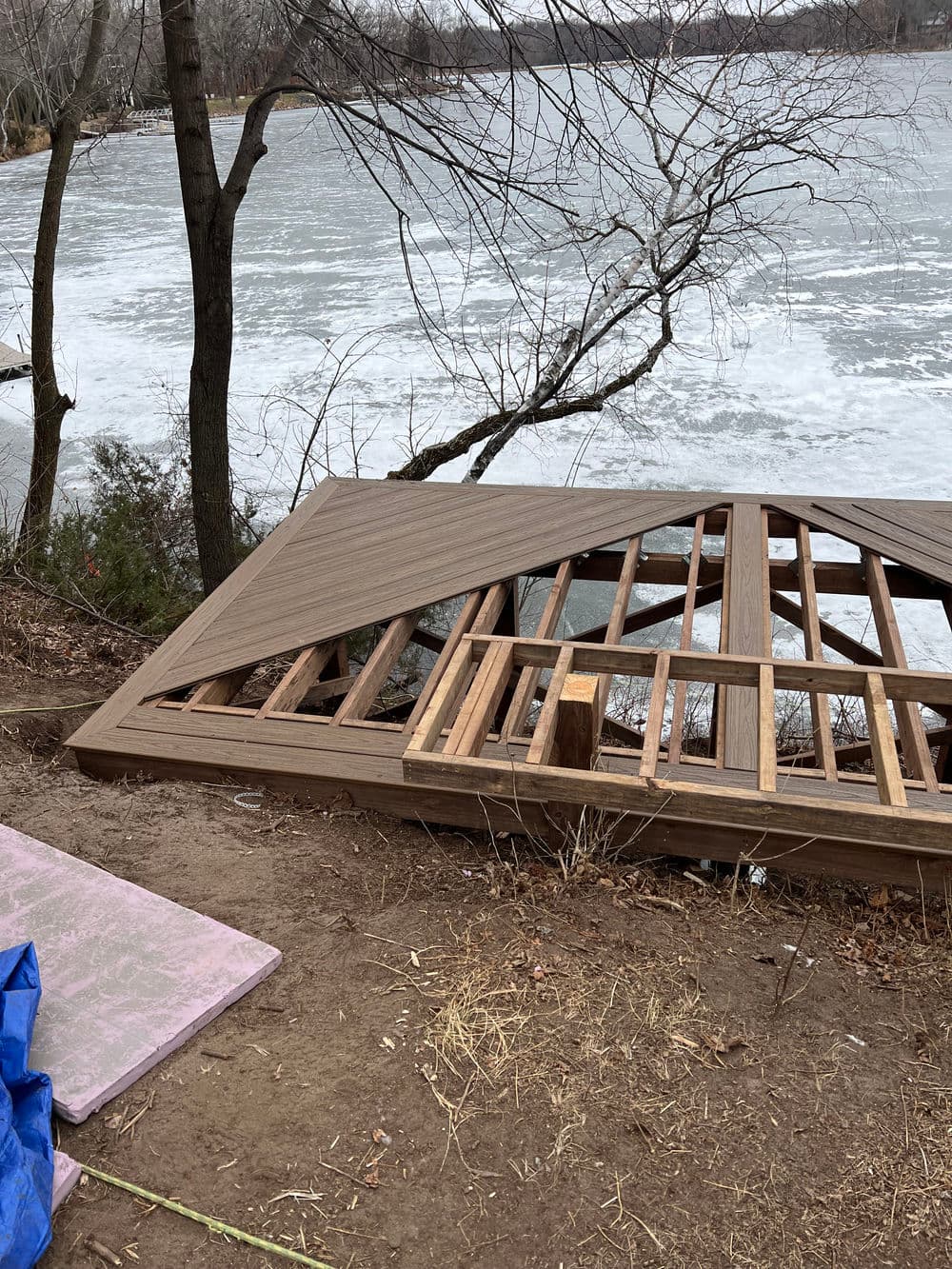 Wooden deck framing under construction near a frozen river in a winter setting.