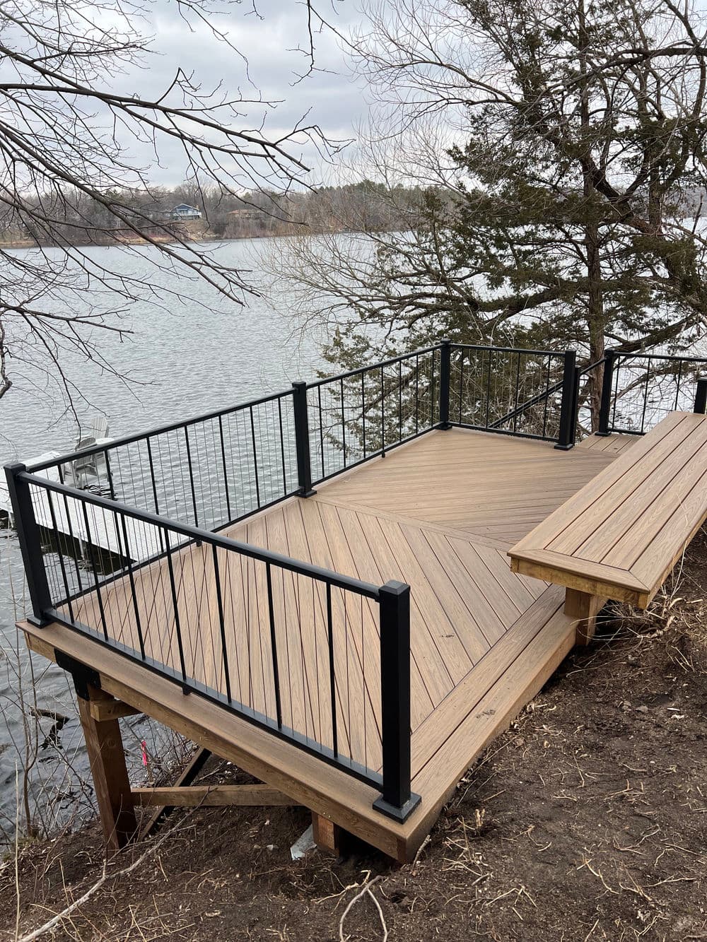 Wooden deck overlooking a river, featuring black railings and a built-in bench.