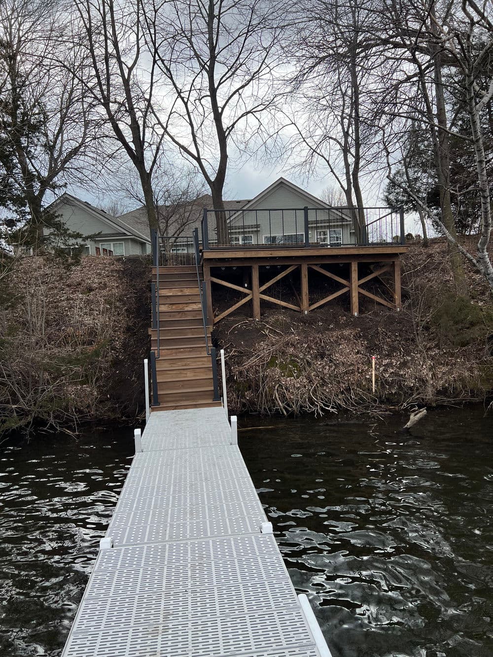 Staircase leading to a lakeside house with a wooden deck and dock on calm water.