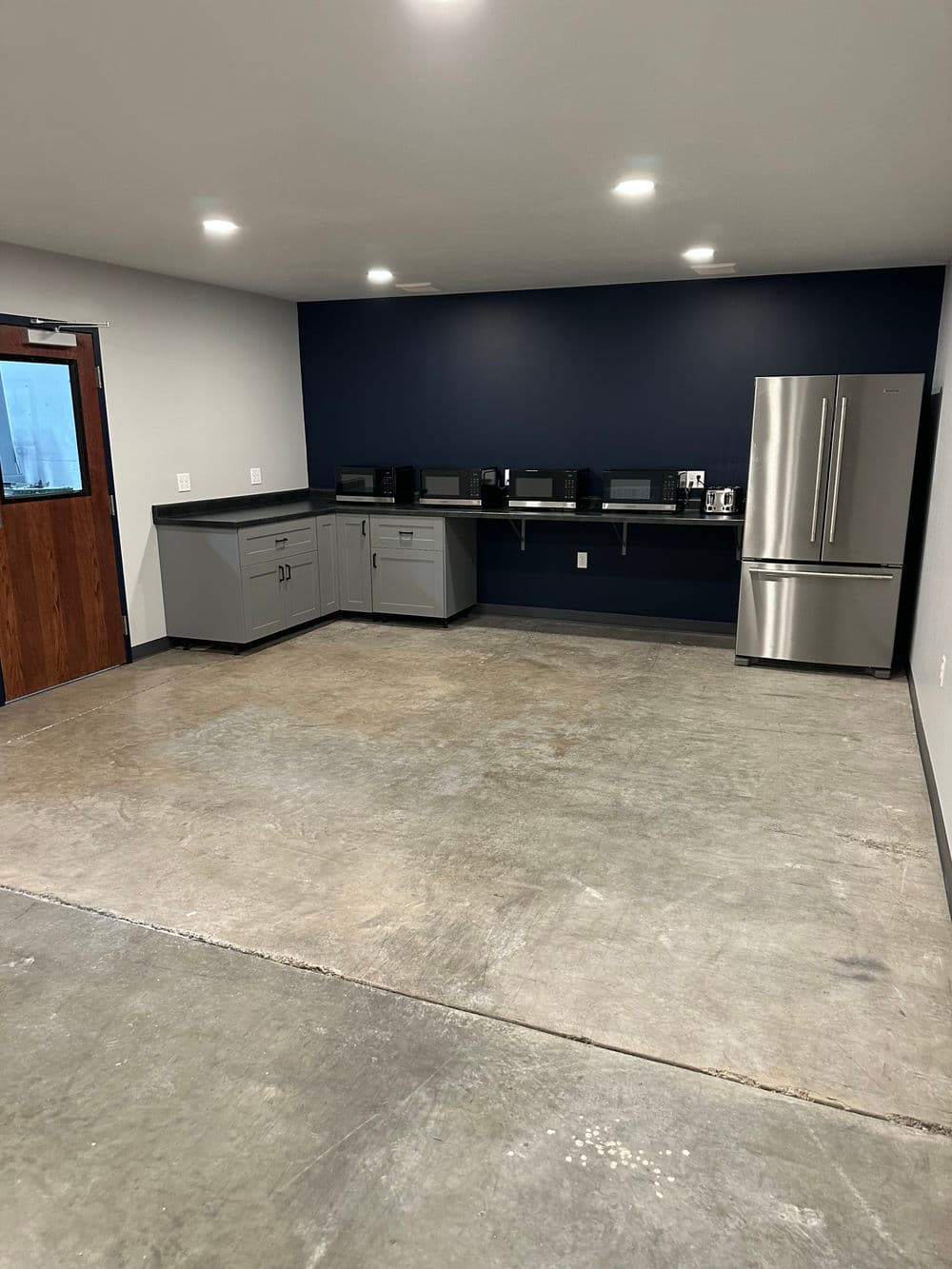 Modern kitchen area with stainless steel appliances, gray cabinets, and concrete flooring.