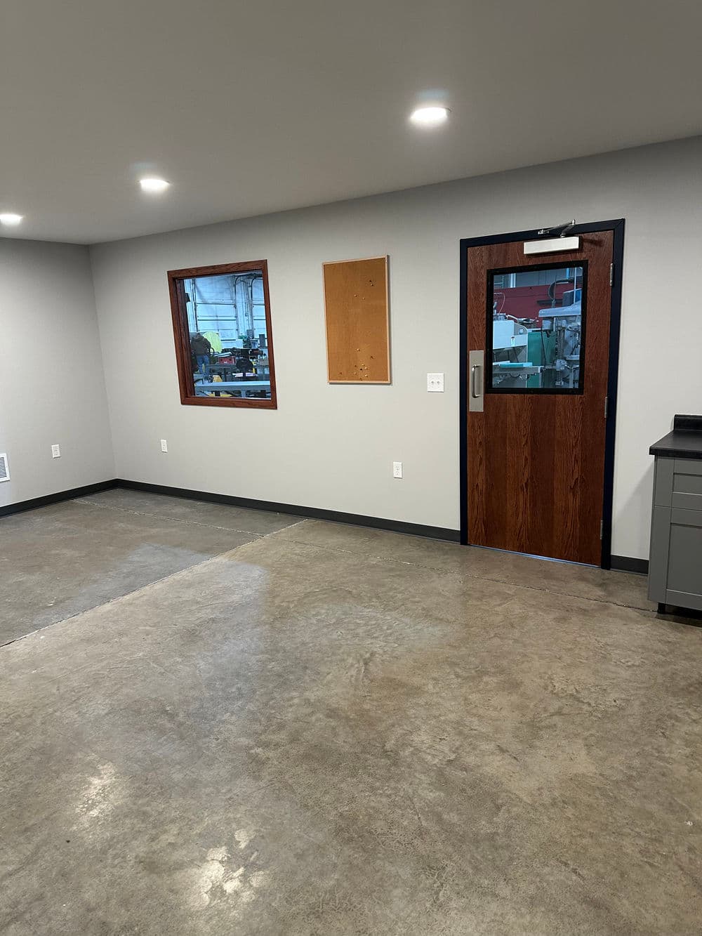 Modern office interior with gray walls, wood door, and concrete floor, featuring a window.
