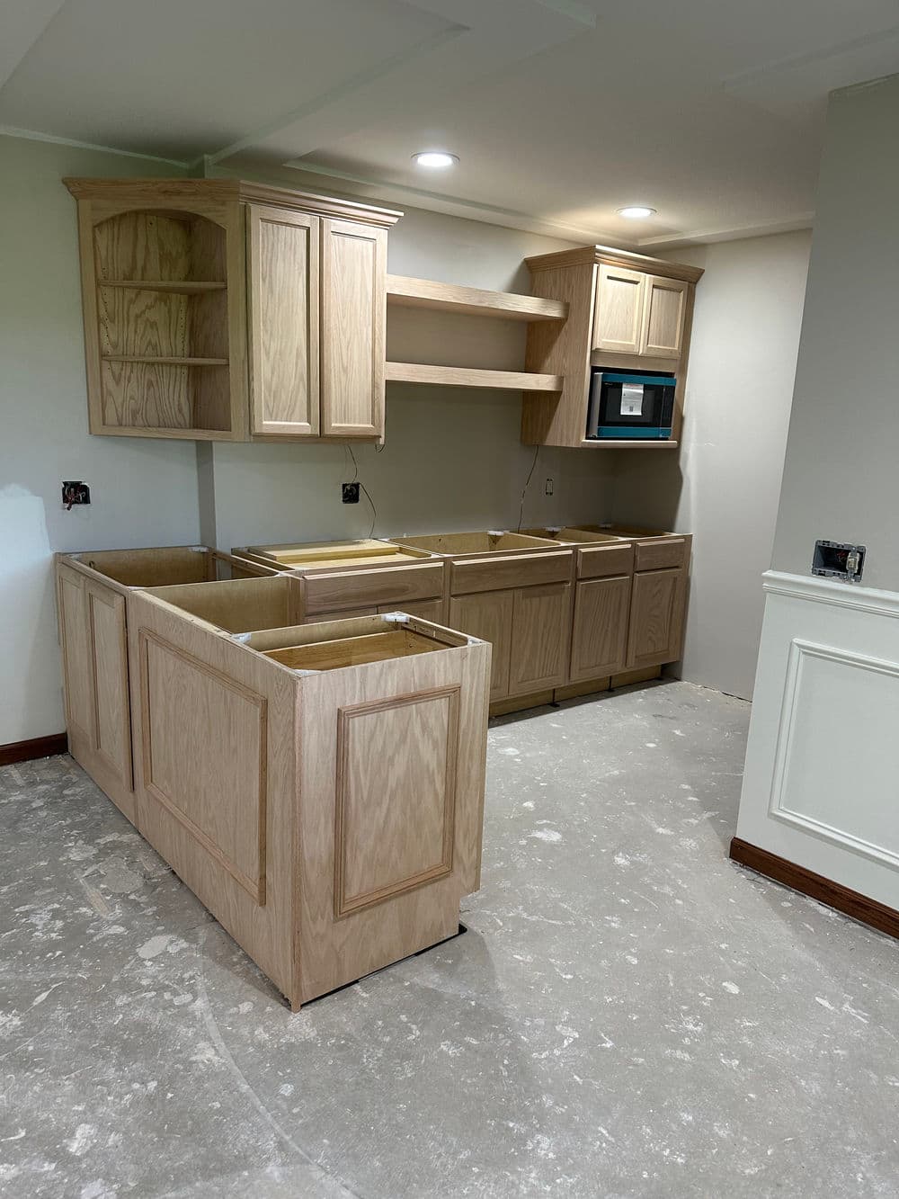 New kitchen cabinetry installation in progress, featuring wooden cabinets and open shelving.