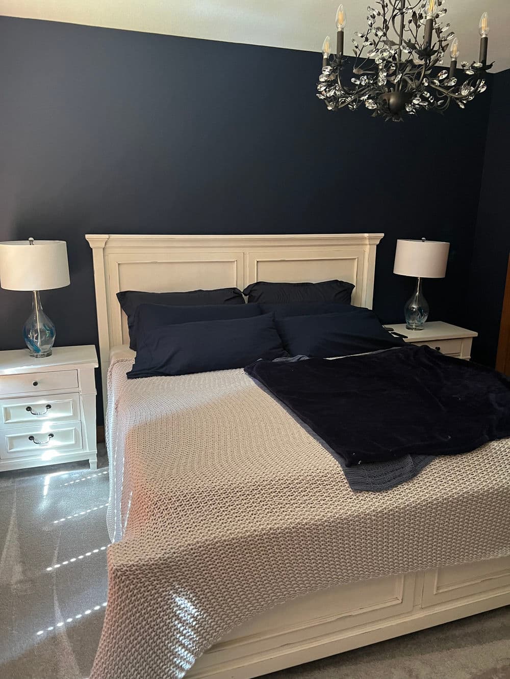 Cozy bedroom with navy walls, white furniture, a chandelier, and elegant bedding.
