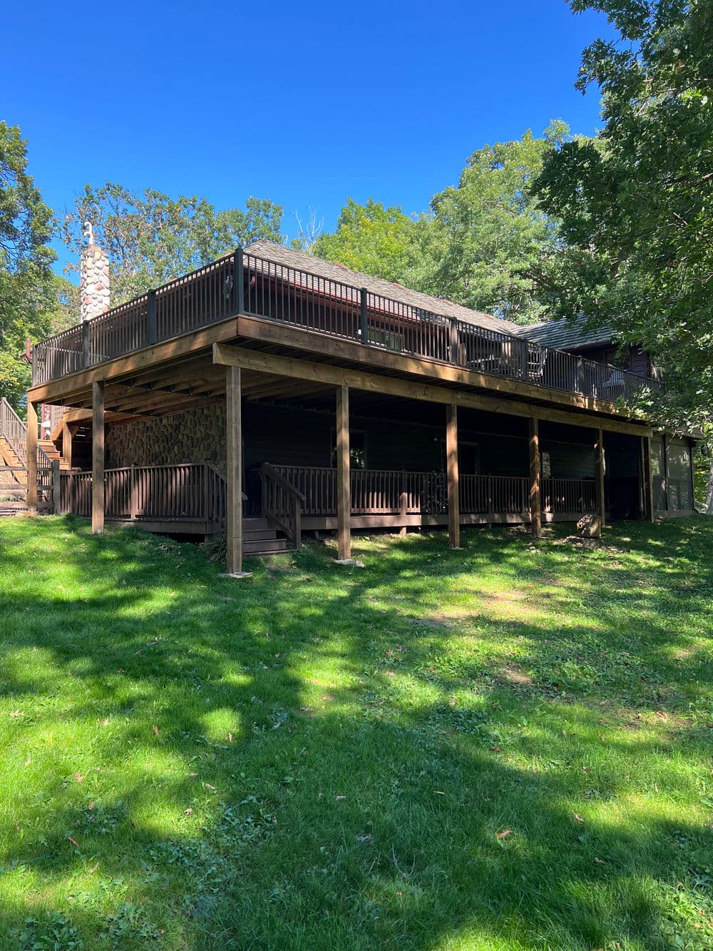 Spacious wooden deck on a house surrounded by greenery under a clear blue sky.
