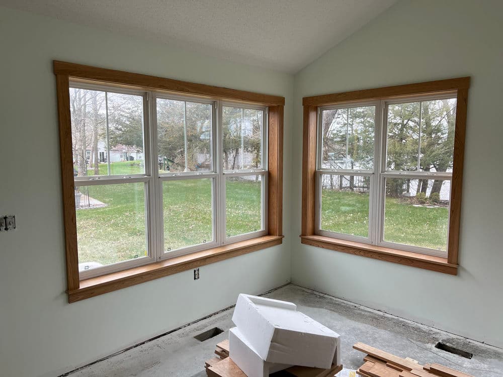Bright, unfinished room with bay windows, wooden trim, and a view of the yard outside.
