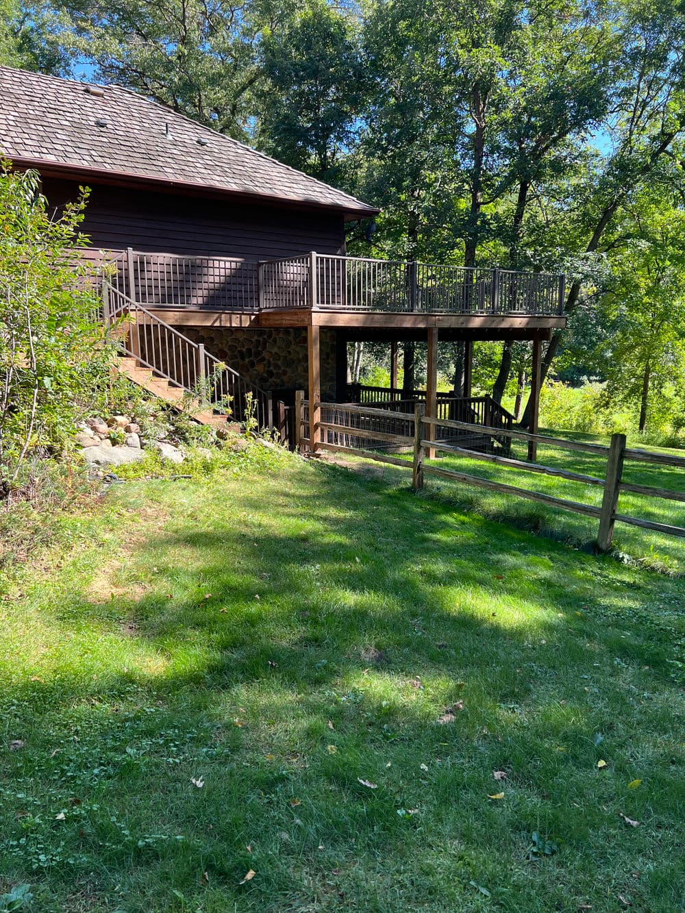 Wooden deck of a house surrounded by greenery and trees on a sunny day.