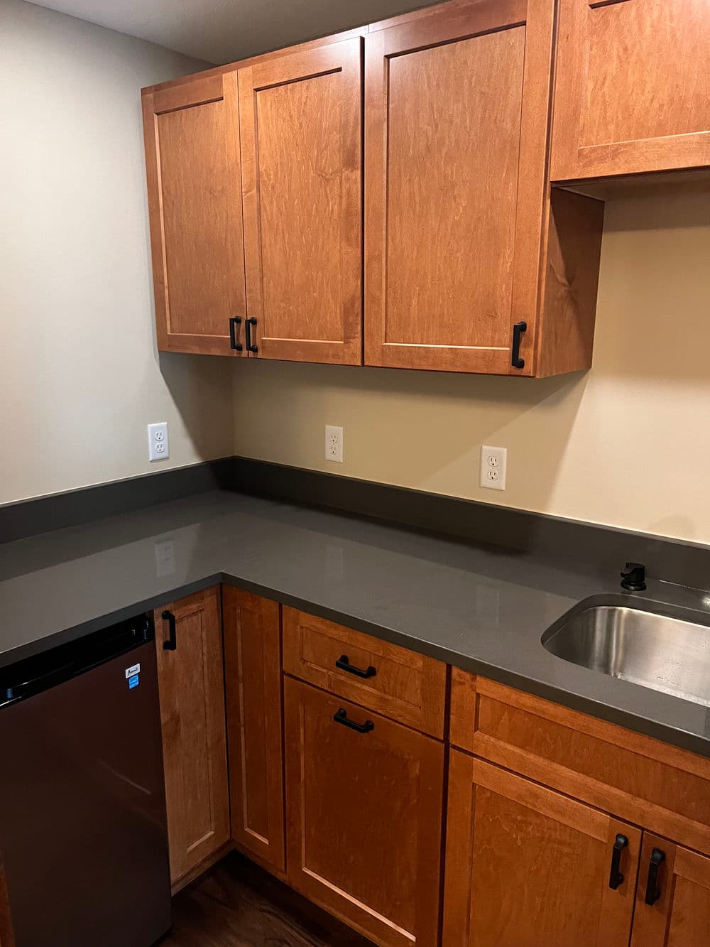Modern kitchen featuring wooden cabinets, gray countertops, sink, and stainless steel fridge.