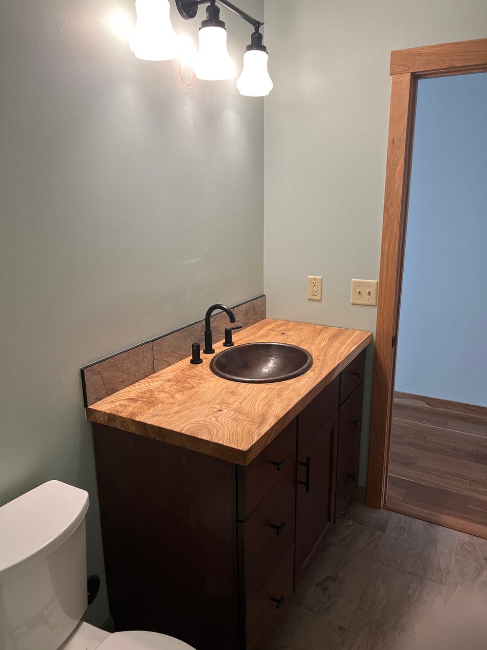 Modern bathroom vanity with a wooden countertop, bronze sink, and stylish light fixtures.