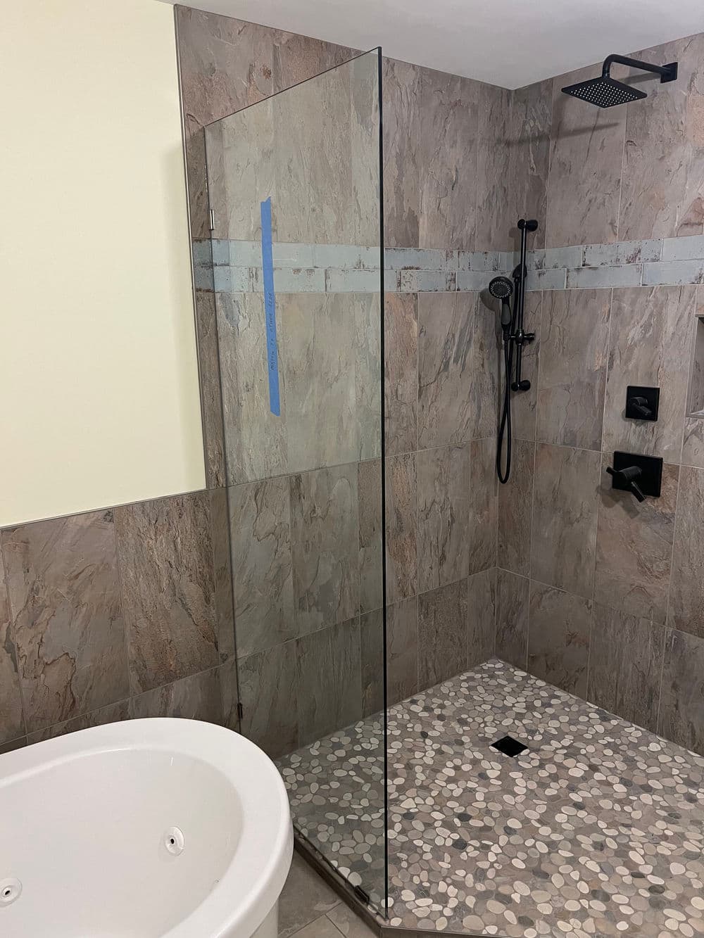 Modern bathroom with glass shower enclosure, stone walls, and pebble floor.
