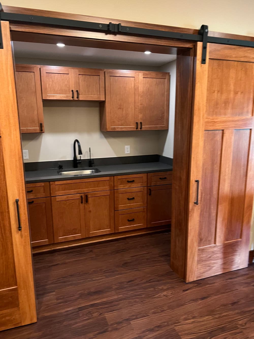 Modern kitchen with wooden cabinets, sleek black countertop, and sliding barn doors.