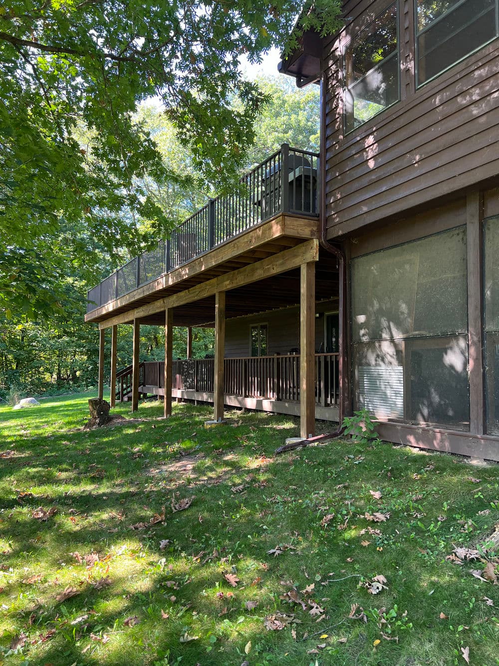 Two-story wooden house with a spacious balcony overlooking a lush green yard.