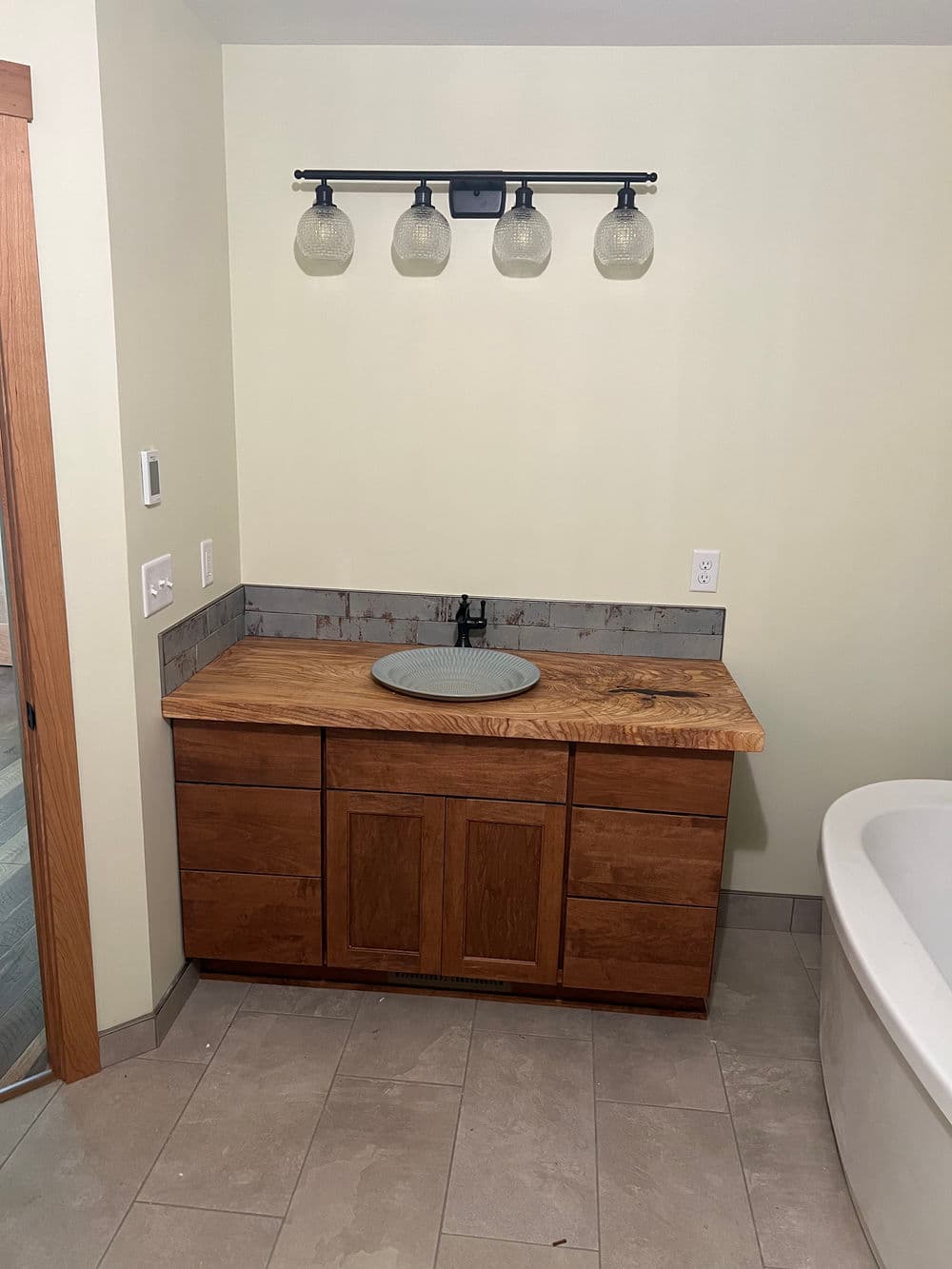 Modern bathroom vanity with wooden cabinetry, circular sink, and stylish light fixtures above.