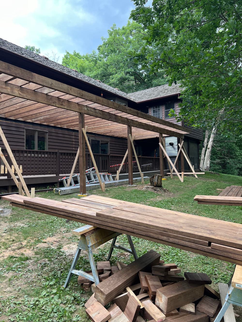 Construction of a wooden deck extension on a rustic house surrounded by greenery.