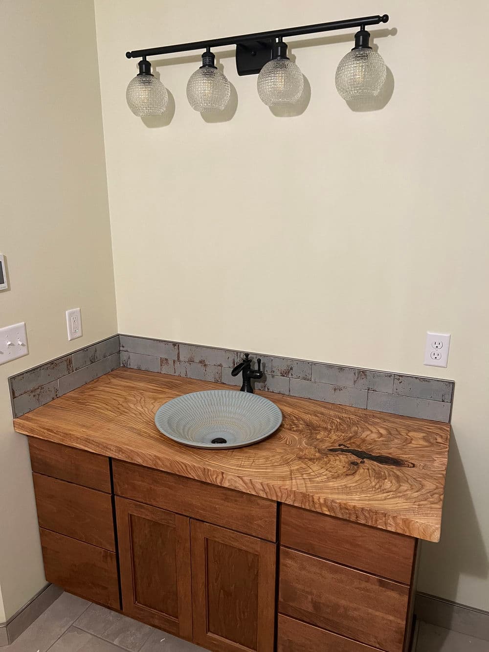 Modern bathroom vanity with wooden countertop, bowl sink, and stylish light fixture.