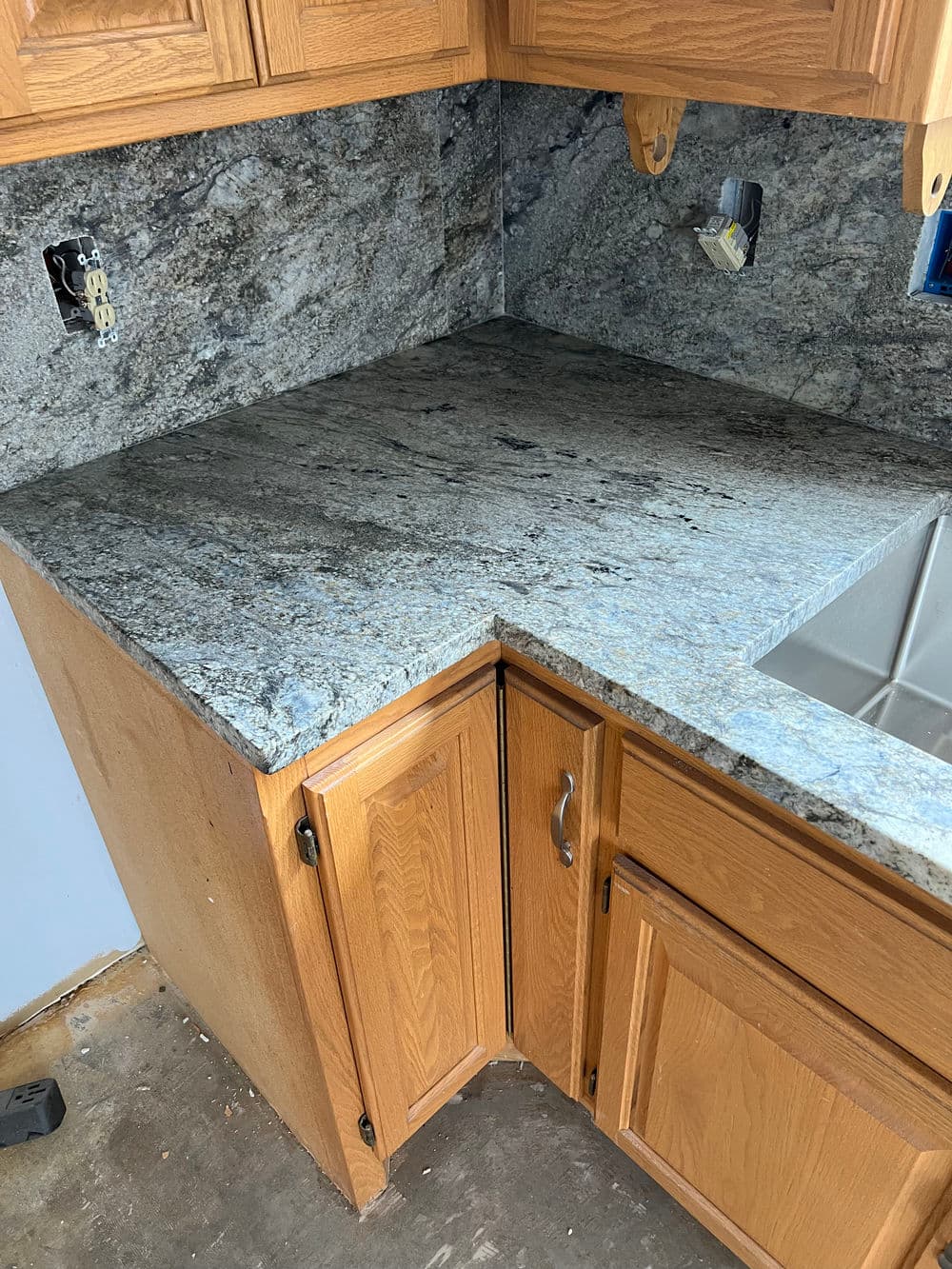 Granite countertop installation in wooden kitchen cabinetry, featuring a corner sink area.