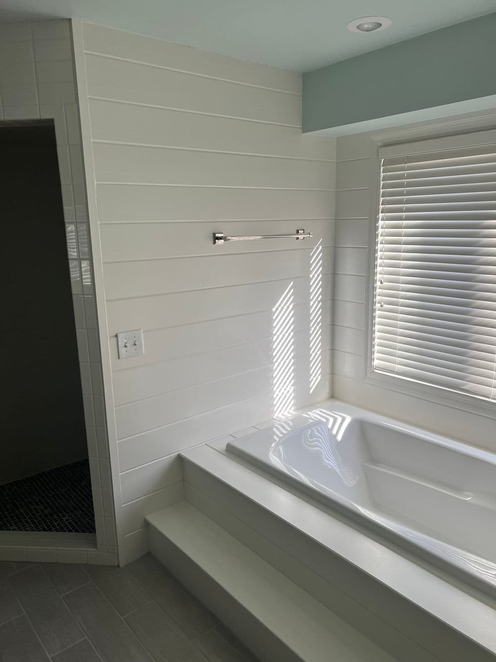 Modern bathroom featuring a soaking tub, white shiplap walls, and natural light from windows.
