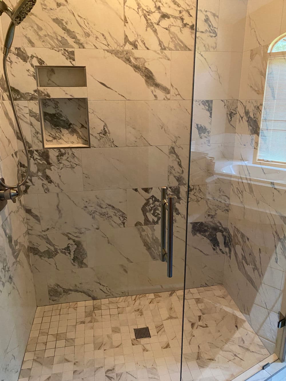 Modern marble shower with glass enclosure and sleek fixtures, featuring a built-in shelf.