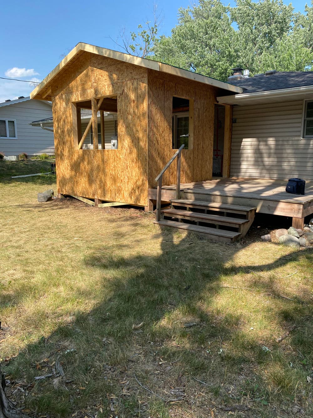 Newly constructed shed with wooden exterior and a small deck in a grassy yard.