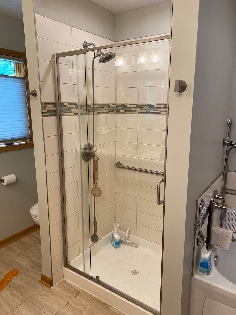 Modern glass shower enclosure with tiled walls and grab bar in a clean bathroom setting.