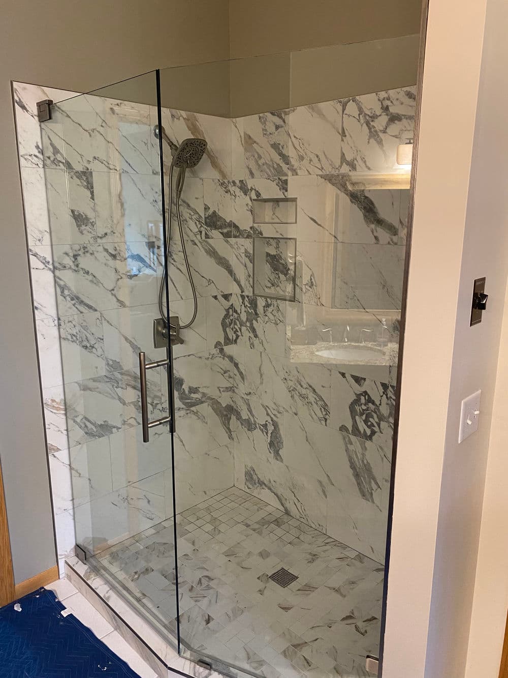 Modern glass shower enclosure with marble tiles and overhead showerhead in a stylish bathroom.