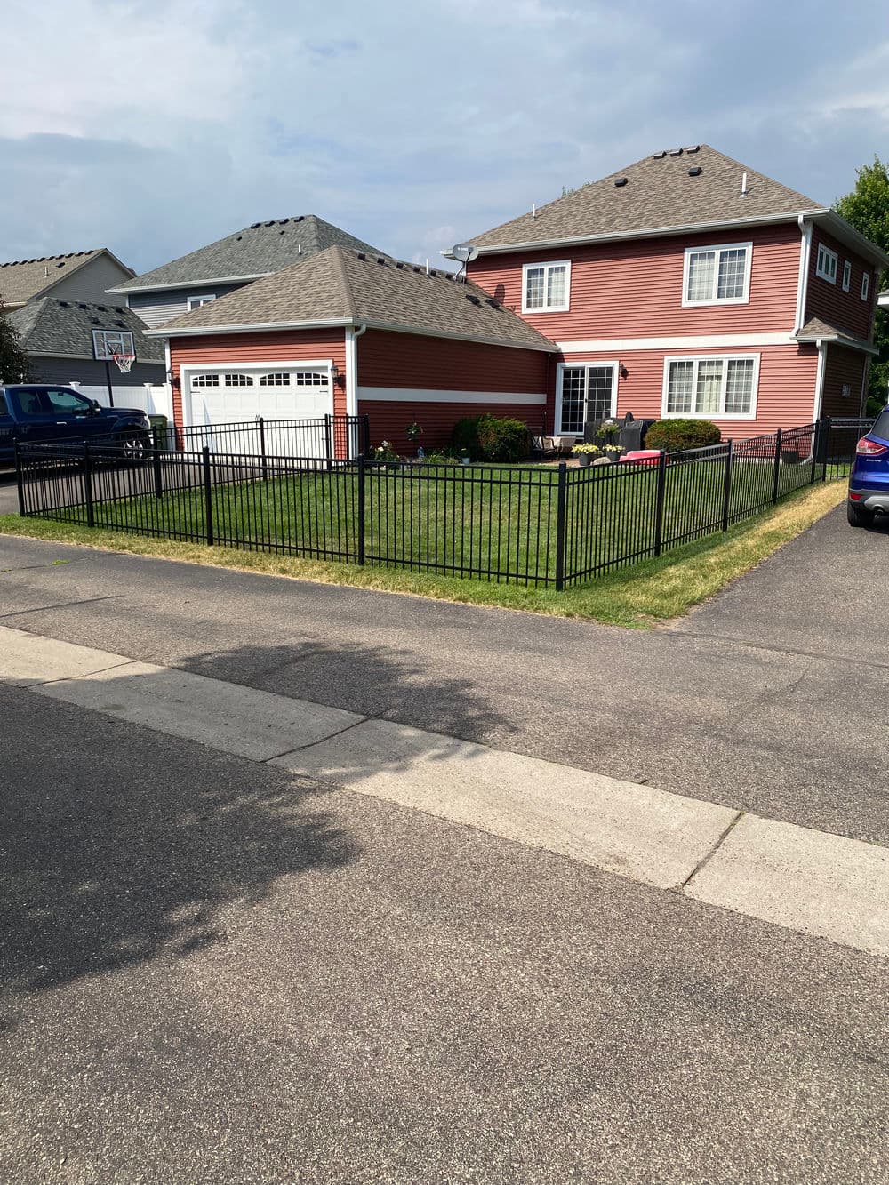 Black metal fence surrounding a landscaped yard of a red two-story house in a suburban neighborhood.