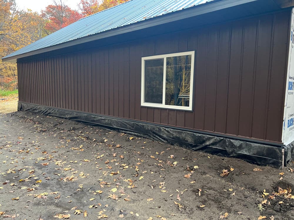 Side view of a newly built brown metal-sided house with a window and bare ground.