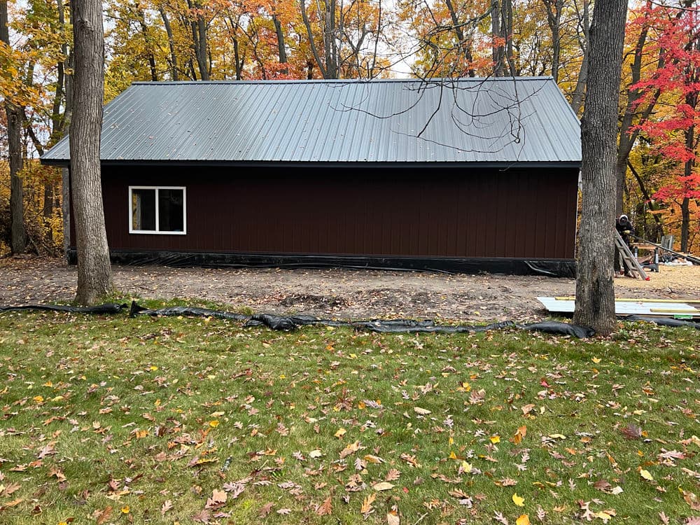 Newly built rustic cabin with a metal roof, surrounded by autumn foliage and grassy area.