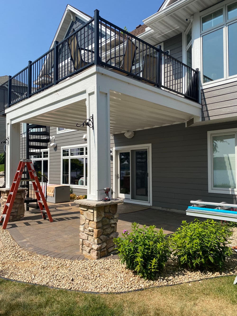 Two-story home exterior with a balcony, stone columns, and a landscaped patio area.