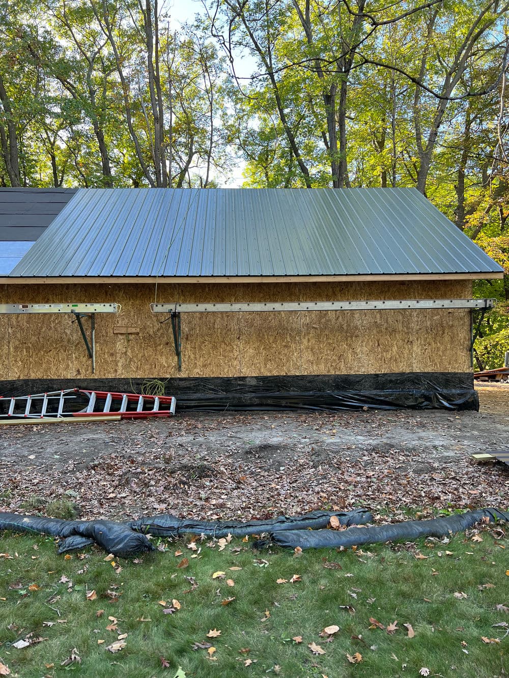 Metal roof installation on a wooden structure surrounded by trees and construction equipment.