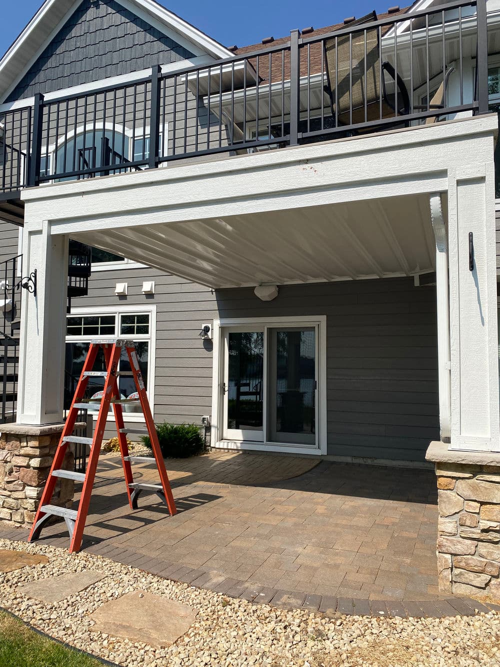 Under-construction patio with a ladder, stone walls, and a covered upper deck area.