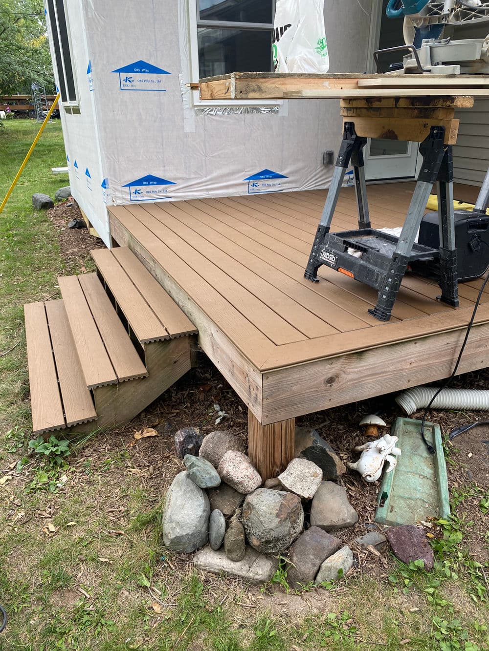 Newly built wooden deck with steps, workbench, and tools in a backyard setting.