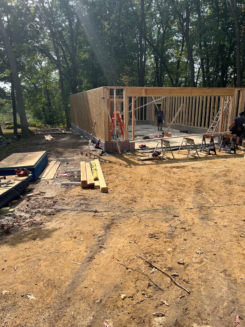 Construction site featuring framed walls and workers in a wooded area.