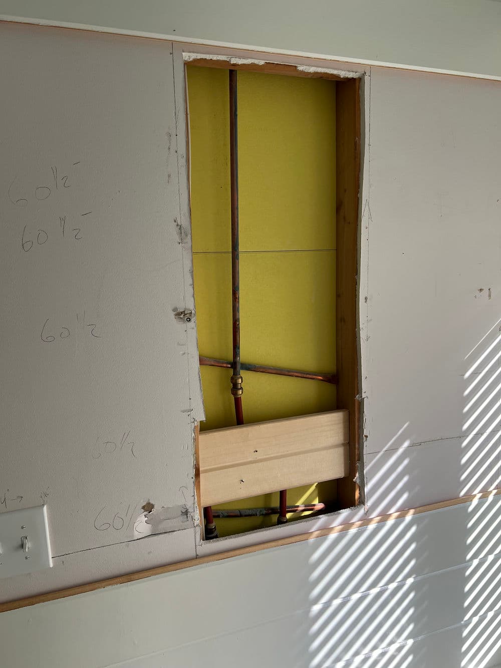 Open wall cavity revealing plumbing and insulation installation with sunlight casting shadows.