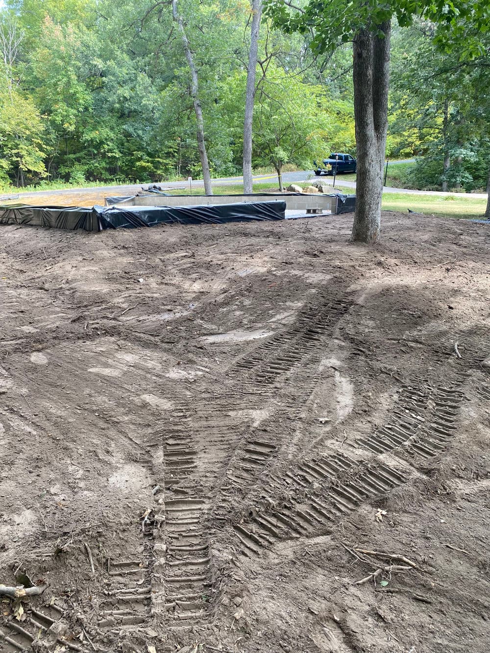 Excavated area with tire tracks, preparing ground for construction amidst trees.