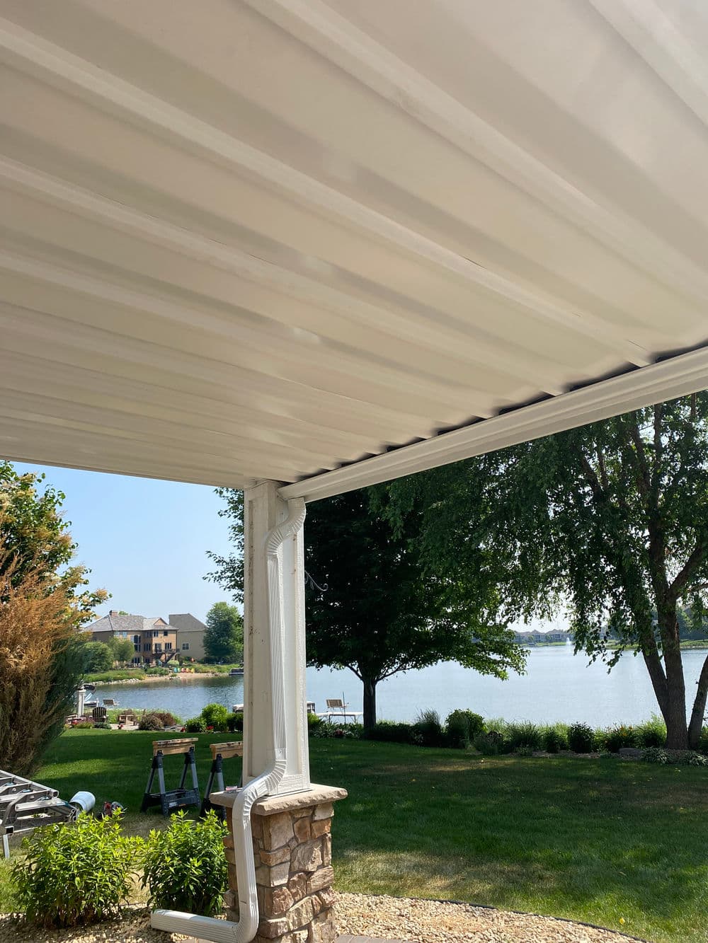 View of a patio awning overlooking a serene lake and lush greenery in a residential area.