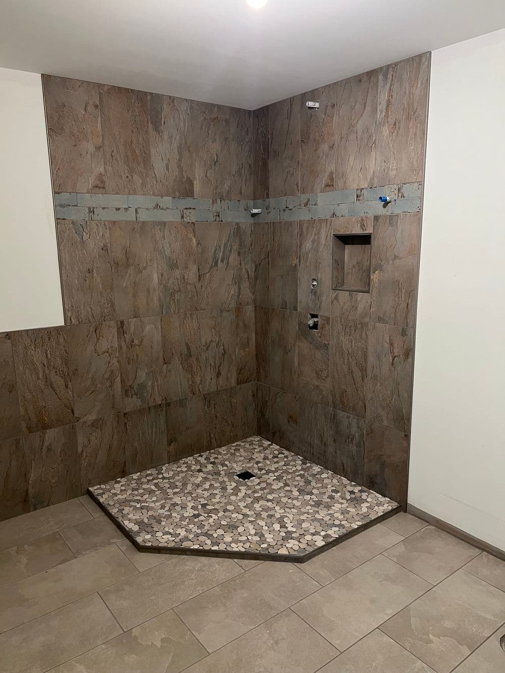 Modern shower installation with stone tiles, featuring an octagonal base and wall fixtures.